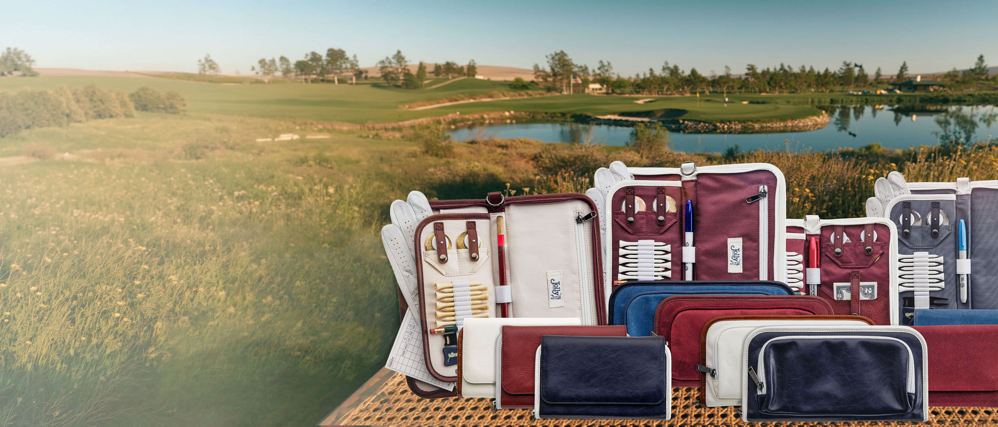 A collection of golf bag organizer pouches in burgundy, navy, and white, arranged on a wooden table against a scenic background of a golf course and a lake.